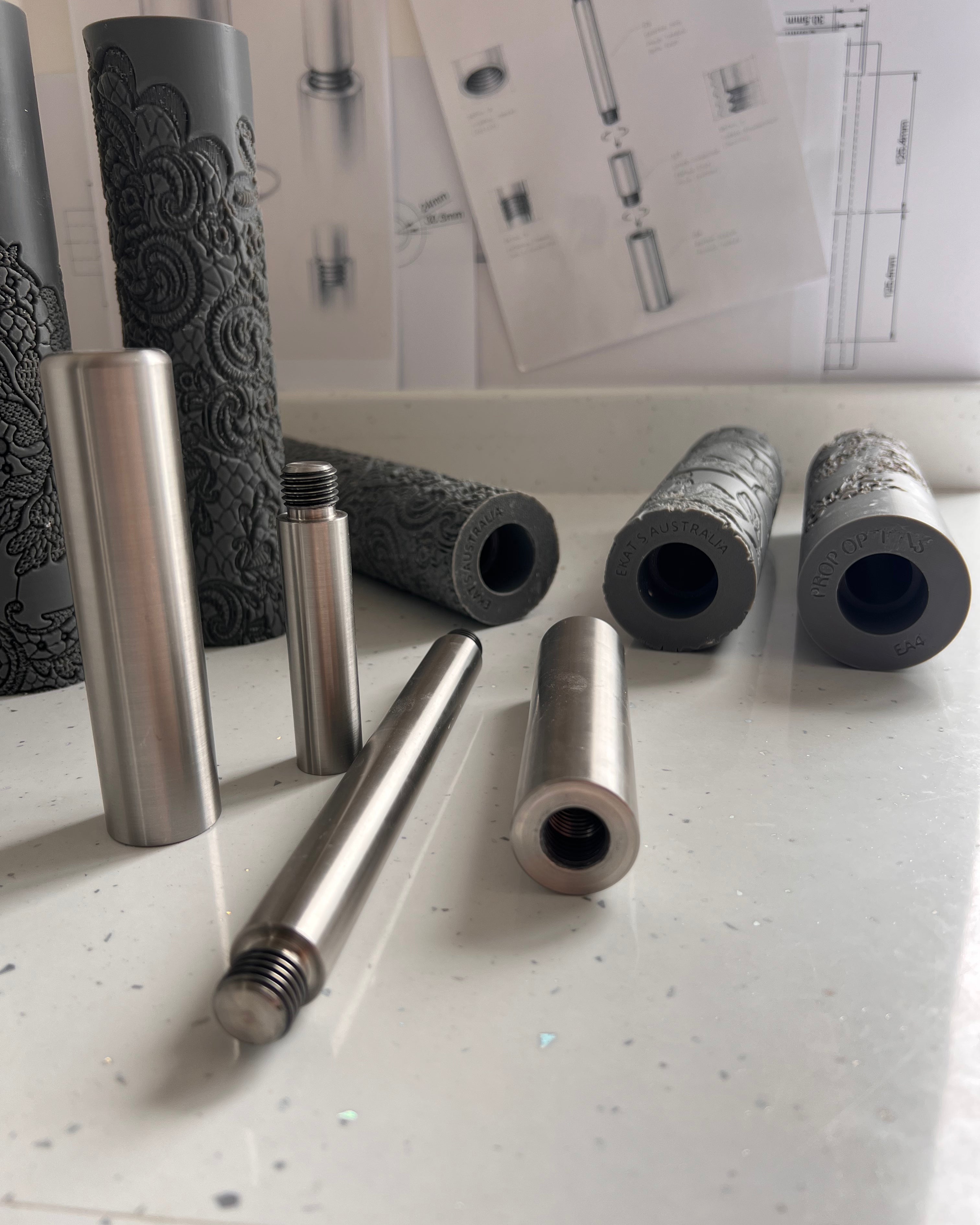 Metal and foam cylindrical objects on a white surface with technical drawings in the background.